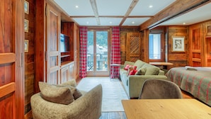 Ein gemütliches Blockhauszimmer mit Holzwänden, einer Couch, einem Tisch und Blick durch eine Glastür.