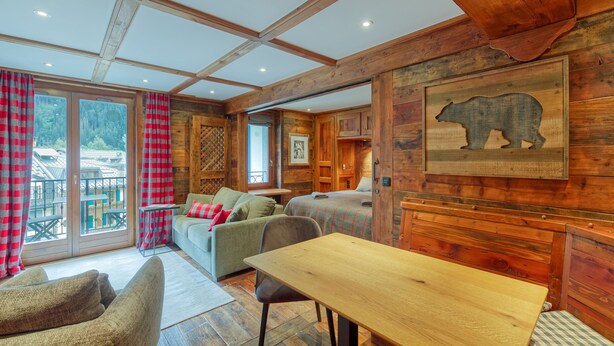 Ein gemütliches Blockhaus-Interieur mit Holzbalkendecke, Esstisch, einer Couch und einem Bett.
