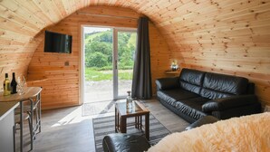 A cozy, wooden-paneled room with a black leather sofa, a small table, and a TV mounted on the wall.