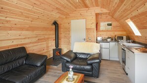 A cozy log cabin interior with a fireplace, leather sofas, a kitchen area, and a loft bedroom with a skylight.
