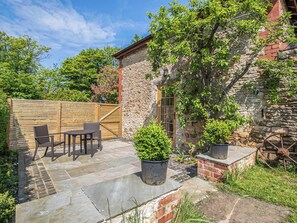 A stone building with a wooden fence, outdoor seating, and potted plants.