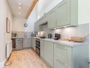 A modern kitchen with light green cabinets, stainless steel appliances, and a wooden floor.