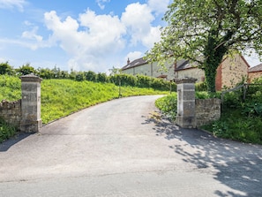 A rural road leading to a stone gate with a house in the background.