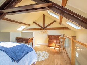 A bedroom with a sloped ceiling, wooden beams, a bed, a dresser, a chair, and a desk.
