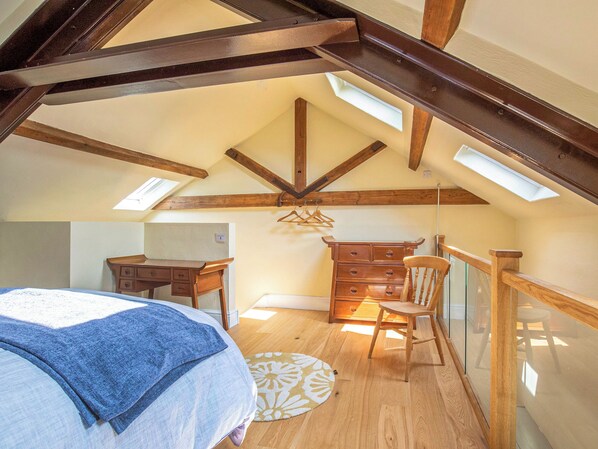 A bedroom with a sloped ceiling, wooden beams, a bed, a dresser, a chair, and a desk. - 1 bedroom accommodation in Dursley (Dursley)