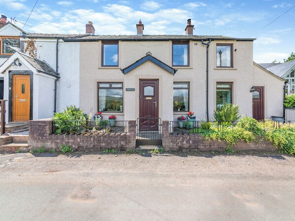 A two-story house with a front door, two windows on the ground floor, and a small porch area with potted plants. - 3 bedroom accommodation in Brampton, near Appleby-in-Westmorland (Brampton, near Appleby-in-Westmorland)