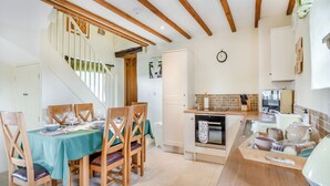 Eine moderne Küche mit Holzbalken, ein Essbereich mit Tisch für vier Personen und eine Treppe zu einer weiteren Ebene.