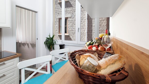 A kitchen with a wooden table, a white chair, a basket of bread, and a window with a view of a stone building. - shinehouse (Sorrento)