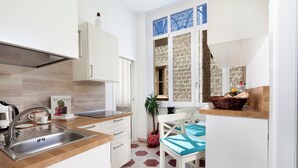 A modern kitchen with a stainless steel sink, white cabinets, and a wooden countertop. There is a window with a view of the outside, and a small table with a basket on it. - shinehouse (Sorrento)
