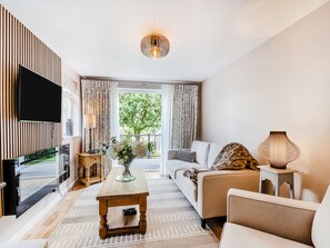 A modern living room with a flat-screen TV, a wooden coffee table, a sofa, and a lamp.