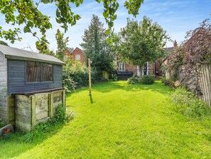 A well-maintained backyard with a wooden shed, a tall tree, and a brick house in the background. - Wheelwright's Cottage (Rodsley, near Ashbourne)