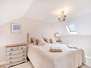 A bedroom with a bed, bedside table, dresser, and a chandelier.