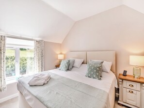 Ein Schlafzimmer mit einem großen Bett, zwei Nachttischen, einem Beistelltisch und einem Fenster mit Vorhängen.