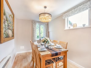 A dining area with a wooden table set for four, a chandelier, and a window with curtains.