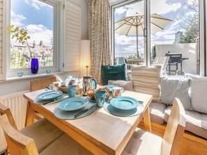 A dining area with a wooden table set for four, a coffee maker, and a view of the city through large windows. - 4 bedroom accommodation in St. Mawes (St. Mawes)