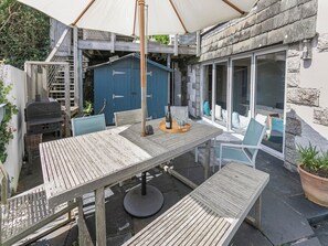 An outdoor patio with a wooden table and chairs, a barbecue grill, and a covered seating area. - 4 bedroom accommodation in St. Mawes (St. Mawes)