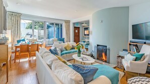 A modern living room with a fireplace, a television, and a dining area with a table and chairs. - 4 bedroom accommodation in St. Mawes (St. Mawes)