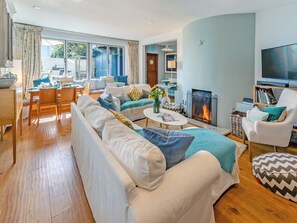 A modern living room with a fireplace, a television, and a dining area with a table and chairs. - 4 bedroom accommodation in St. Mawes (St. Mawes)