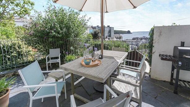 An outdoor patio with a table and chairs, a grill, and a view of the sea. - 4 bedroom accommodation in St. Mawes (St. Mawes)