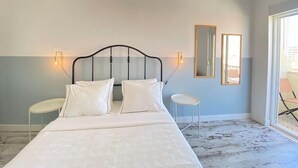 A bedroom with a bed, two bedside tables, a mirror, and a large window. - Apartamento Gertrudes (Setúbal)