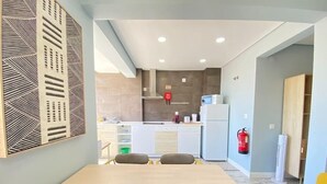 A modern kitchen with a central island, white cabinets, and a microwave. There is a dining table with chairs in the foreground. - Apartamento Gertrudes (Setúbal)