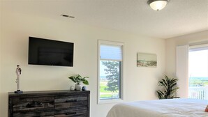 A bedroom with a bed, a dresser, a television, a window with a view, and a plant. - Surfside Beach Cottage- steps from Virginia Beach Boardwalk! (Virginia Beach)