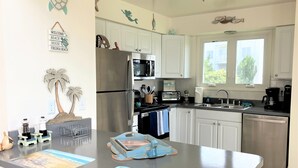 A kitchen with white cabinets, stainless steel appliances, and a central island with two placemats. - Surfside Beach Cottage- steps from Virginia Beach Boardwalk! (Virginia Beach)