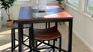 A dining area with a wooden table and chairs, a ceiling fan, and large windows offering views of the neighborhood. - Surfside Beach Cottage- steps from Virginia Beach Boardwalk! (Virginia Beach)
