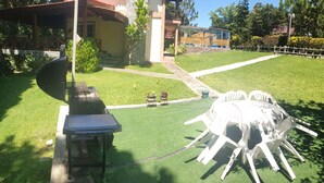 Un patio con una parrilla, una mesa y sillas de exterior, y un pequeño jardín con plantas en macetas.