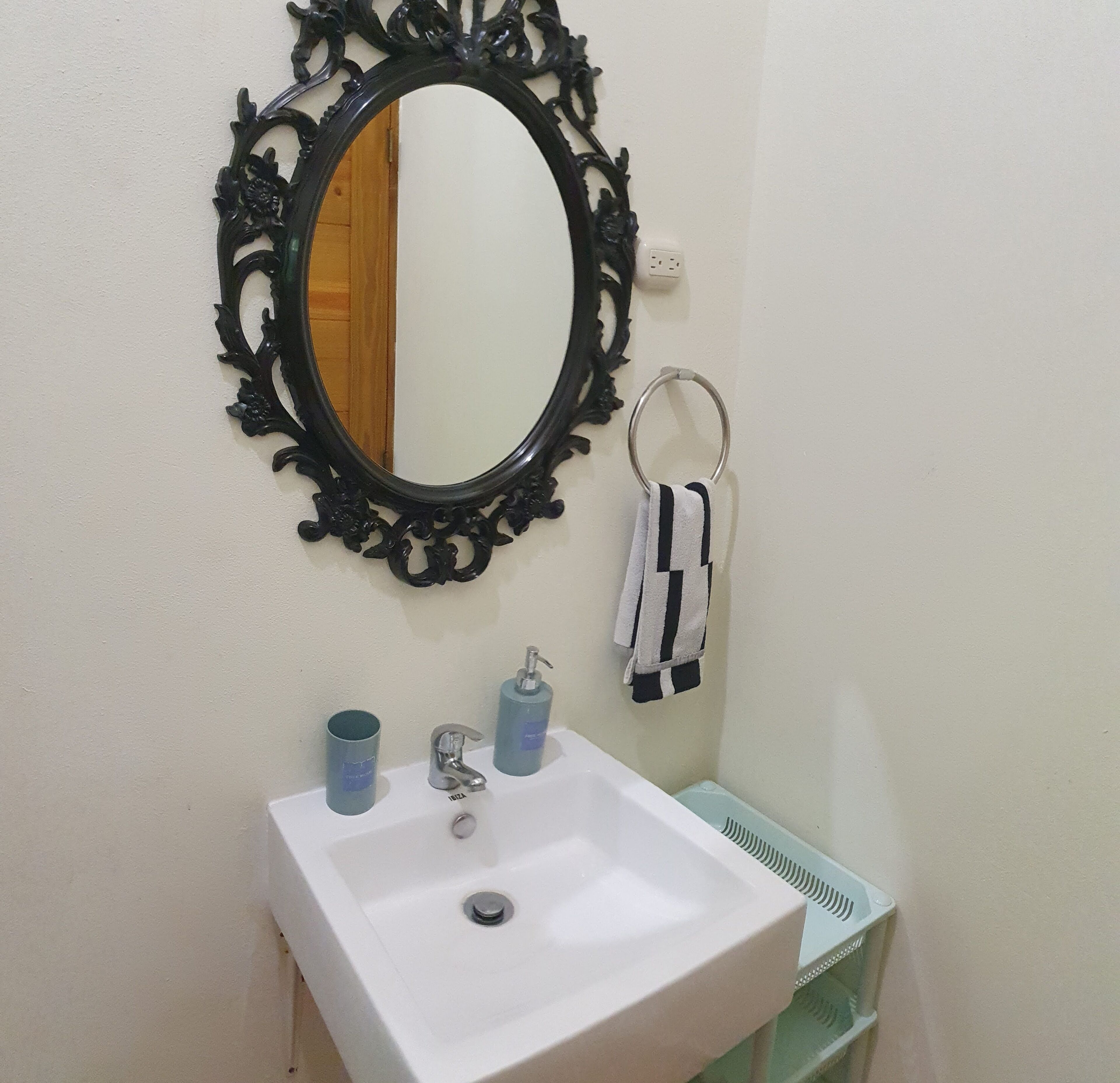 A bathroom with a white sink, a black ornate mirror, a towel ring, and two blue dispensers.