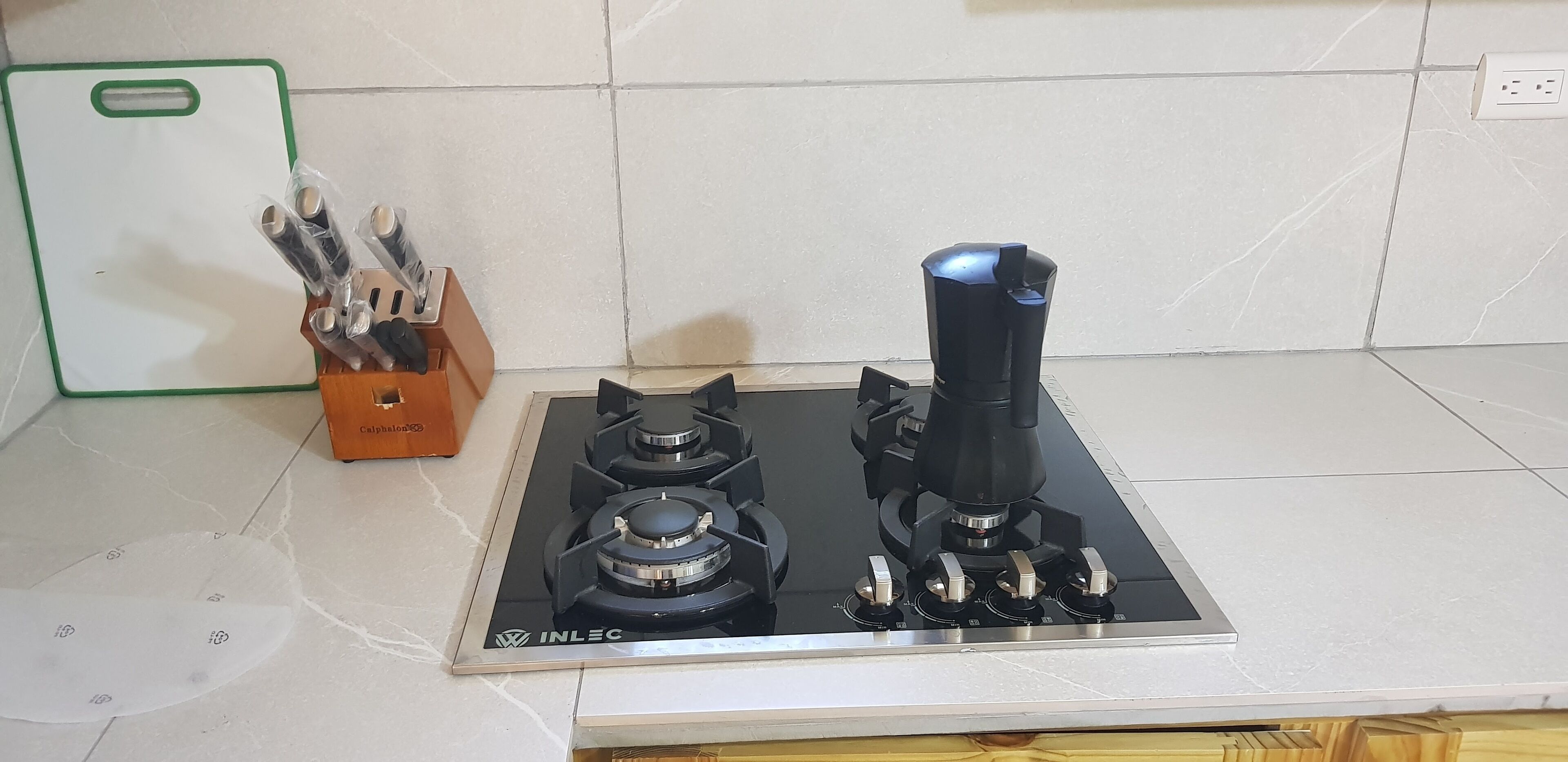 Une cuisine équipée d’une cuisinière à gaz INLEC noire, d’une planche à découper verte et d’un bloc à couteaux.