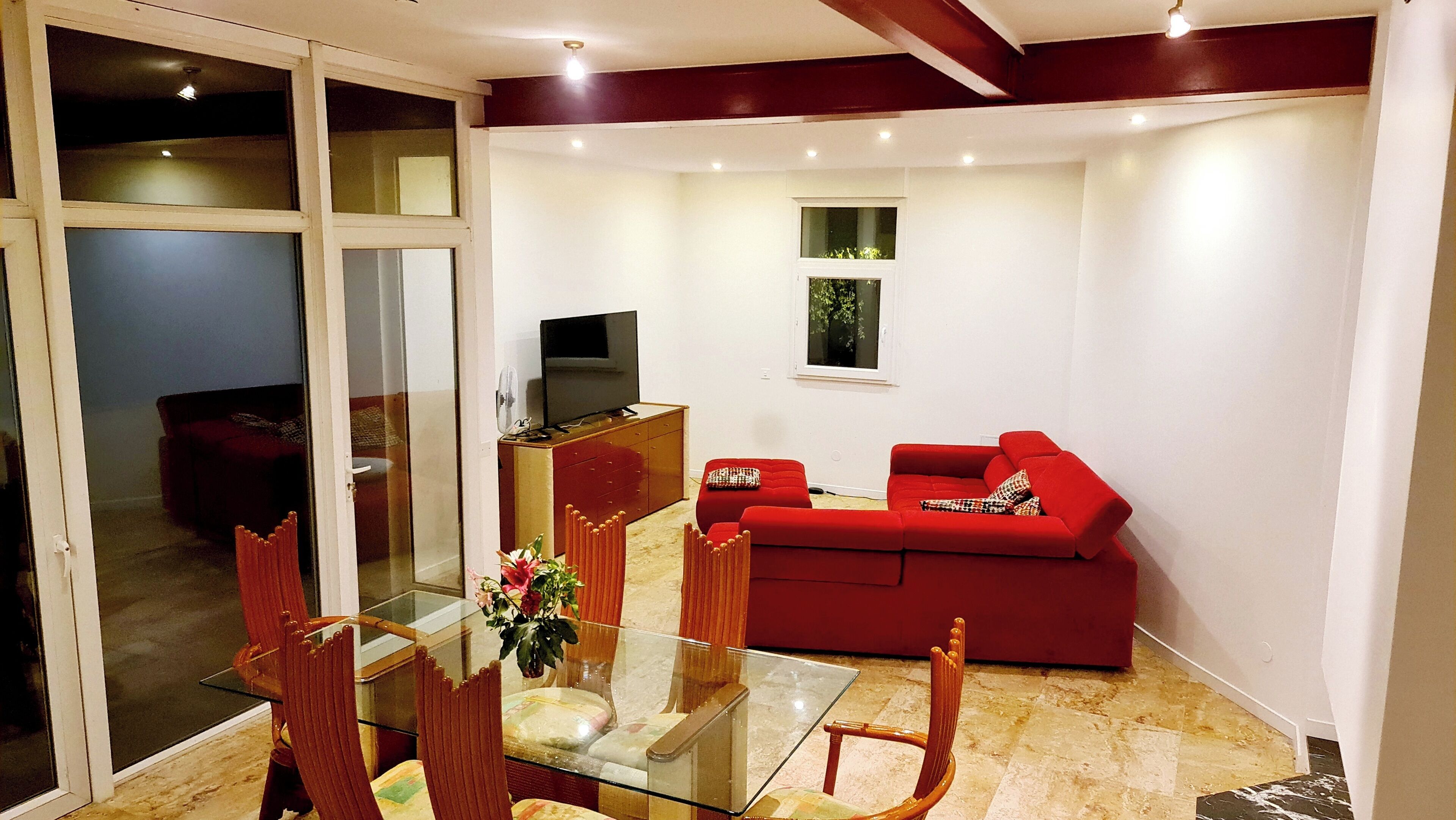 A living room with a glass dining table, red sofa, and a television on a wooden cabinet.