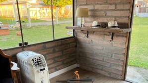 A corner room with a brick wall, a window, and a fan. - Garden house with two bedrooms (Tramandaí Tramandaí)