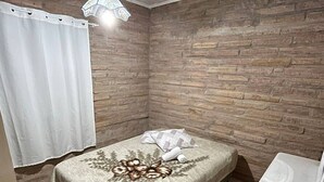 A bedroom with a bed, a small bedside table, a hanging light fixture, and a brick-patterned wall. - Garden house with two bedrooms (Tramandaí Tramandaí)