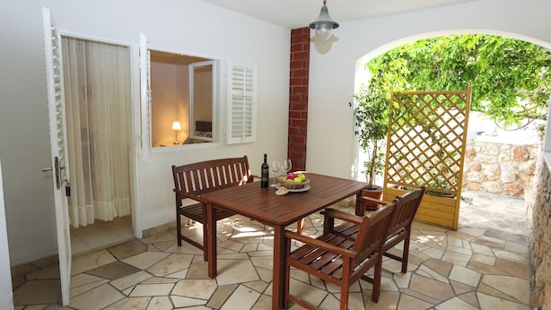 A wooden dining table with chairs, a basket of fruit, a bottle, and a wine glass. - Green Garden Apartment (Hvar)