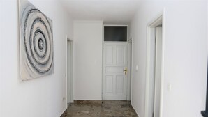 A hallway with a white door, a painting on the wall, and a tiled floor. - Green Garden Apartment (Hvar)
