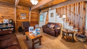 L’intérieur chaleureux d’un chalet avec un plafond en bois, un canapé en cuir, une table basse en bois et un fauteuil en cuir.