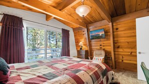 Une chambre avec un grand lit, des poutres apparentes en bois au plafond, une fenêtre avec des rideaux, un tableau au mur et une porte.