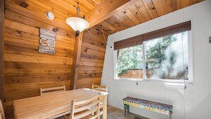 L’intérieur d’un chalet en bois comprend une table à manger, des chaises, un banc et une fenêtre avec des stores.