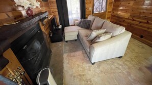 Interior acollidor d'una cabana amb una llar de foc, un sofà i una televisió.