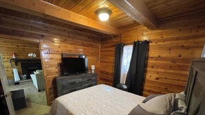 Habitació d'una cabana de fusta amb un llit, un taulell, una televisió i una llar de foc.