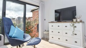 Een moderne woonkamer met een groot raam, een blauwe stoel, een witte dressoir en een flatscreen televisie.