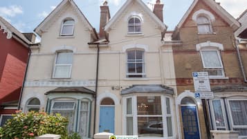 Classic two-story building with a bay window and dormer window, featuring a blue door and a small garden.