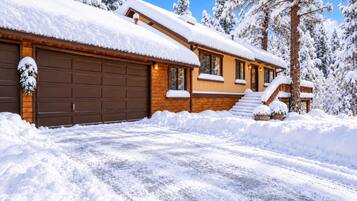 A snow-covered house with a garage, a front porch, and a staircase leading to the entrance.