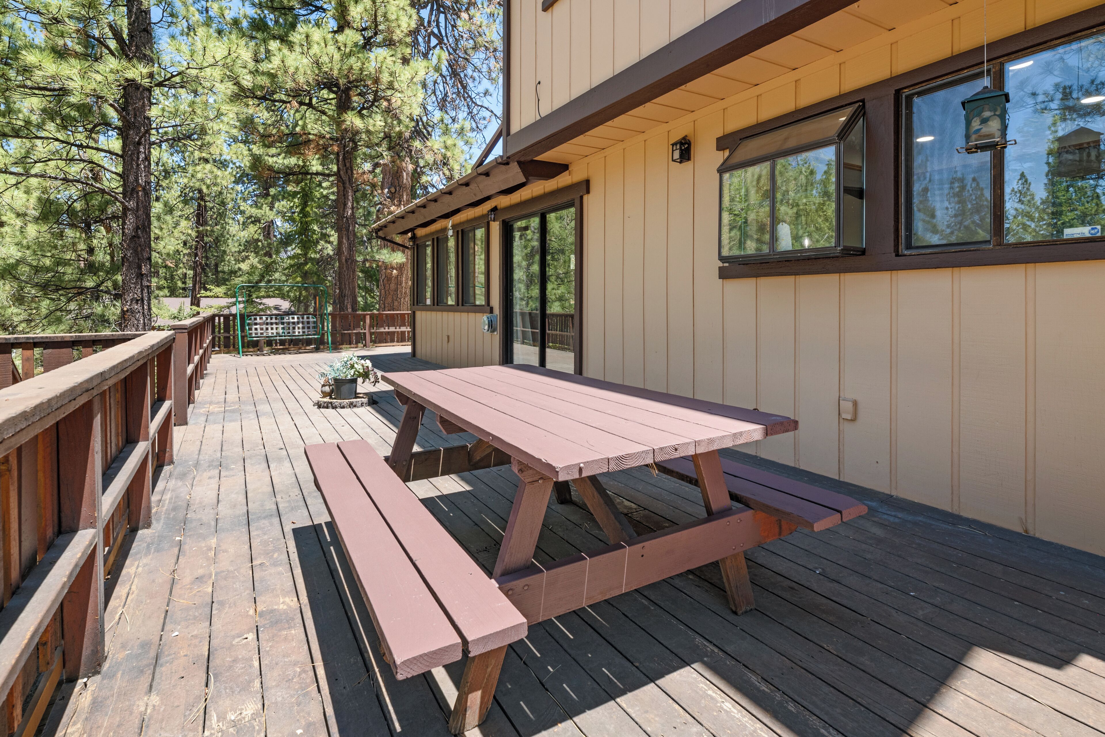 Una terraza de madera con mesas de picnic, rodeada de árboles.