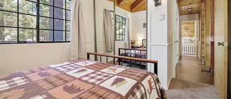 Quarto com cama grande, janela com cortinas, teto de madeira e vista para um deck por uma porta aberta.
