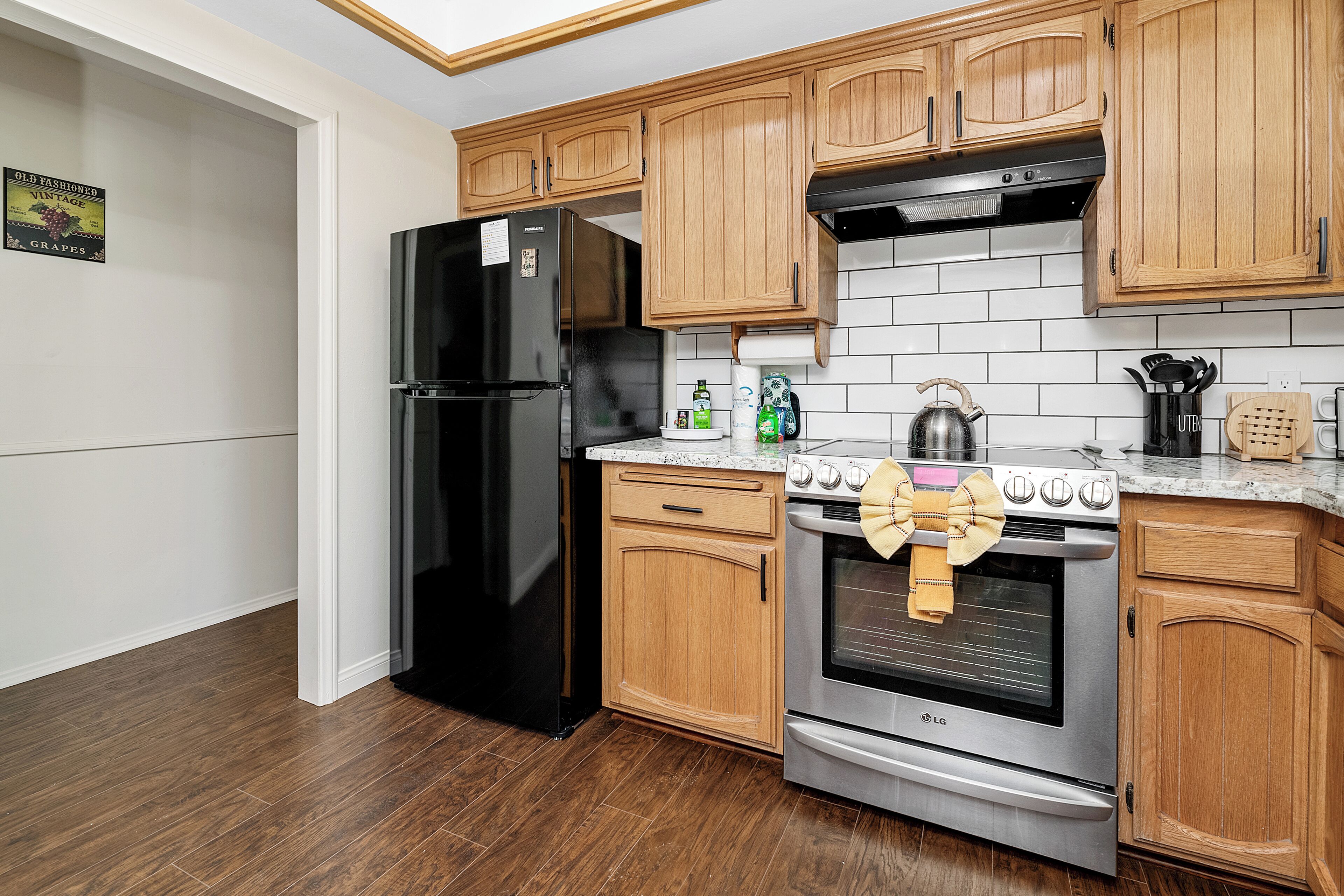 A kitchen with wooden cabinets, a black refrigerator, a stainless steel oven, and a tiled backsplash.