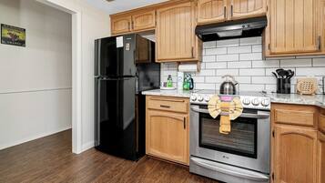 A kitchen with wooden cabinets, a black refrigerator, a stainless steel oven, and a tiled backsplash.