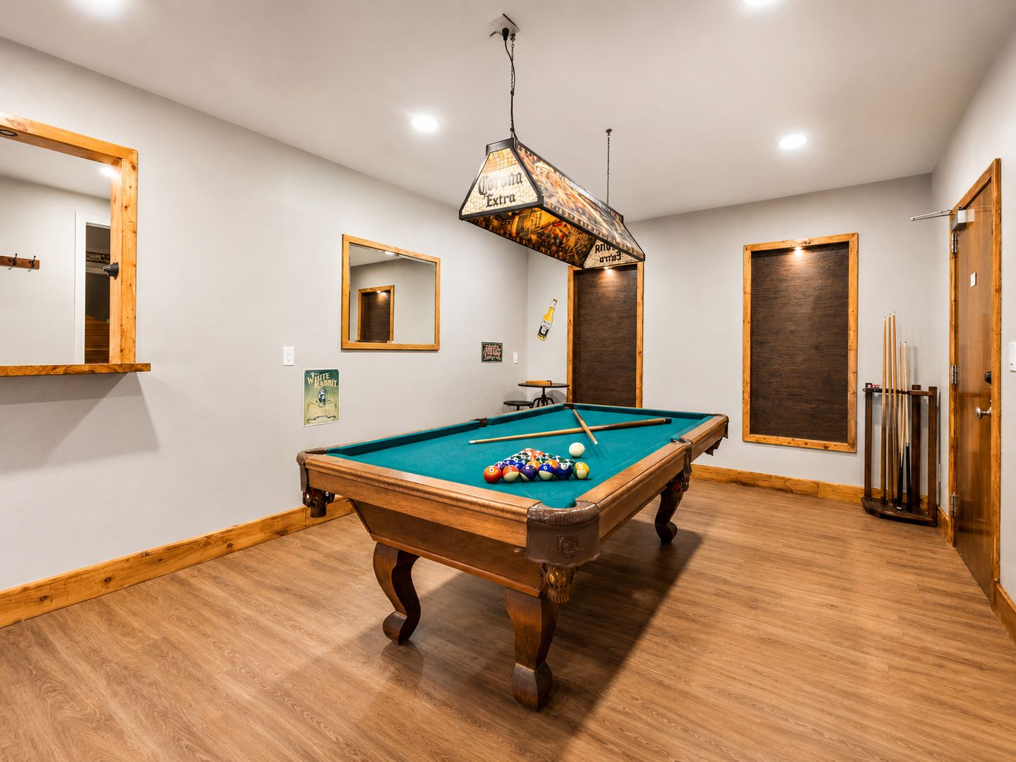 Una mesa de billar en una habitación con piso de madera, un espejo y una puerta con marco de madera.