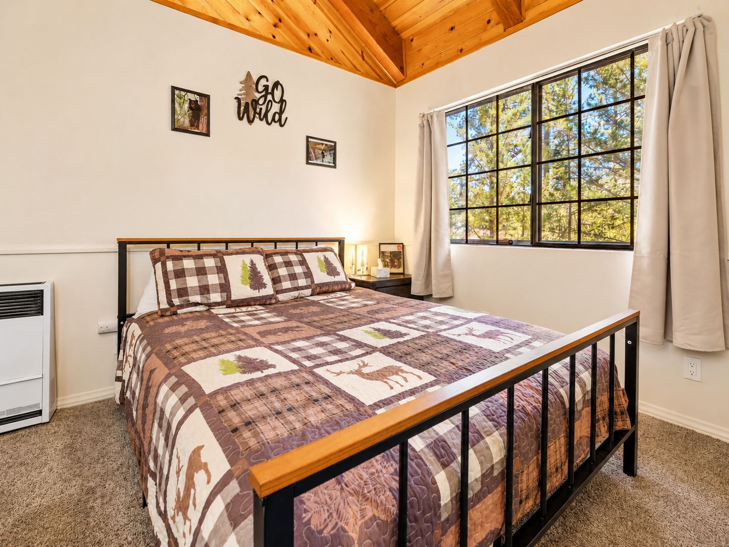 Un dormitorio con una cama grande, una ventana con cortinas, un calentador fijado a la pared y un cartel que dice 'Go Wild'.